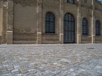 the sidewalk is paved with stones and has a bench in front of it, with no people inside