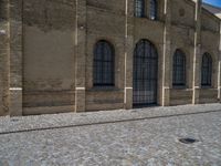 the sidewalk is paved with stones and has a bench in front of it, with no people inside