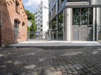 a brick paved street next to buildings on a sunny day that contains a parking lot, and trees