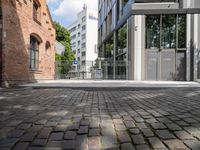 a brick paved street next to buildings on a sunny day that contains a parking lot, and trees