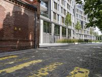 the sidewalk has yellow paint on it and an empty building in the background with trees