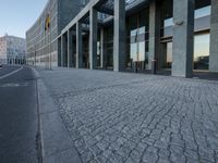 a building with a sidewalk with several stone pavers on it and people walking by