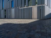 cobblestone driveway surrounded by modern buildings on sunny day with sun reflecting onto the windows