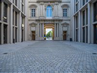 an empty brick courtyard area with two stone columns and two arched windows in the background