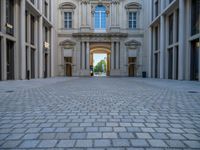 an empty brick courtyard area with two stone columns and two arched windows in the background