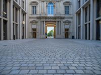 an empty brick courtyard area with two stone columns and two arched windows in the background