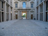 an empty brick courtyard area with two stone columns and two arched windows in the background