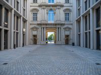 an empty brick courtyard area with two stone columns and two arched windows in the background