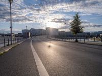 a motorcycle is going down the road by the water at sunset, next to an empty street