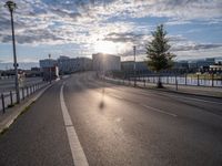 a motorcycle is going down the road by the water at sunset, next to an empty street