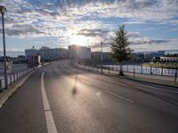 a motorcycle is going down the road by the water at sunset, next to an empty street