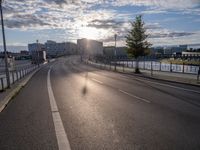 a motorcycle is going down the road by the water at sunset, next to an empty street