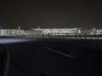 night photo of an empty street in front of the large building and city skyline in the background
