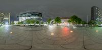 a wide angle shot of a city square at night shows the circular plaza in the middle, with many buildings to one side and lots of the streets on either side