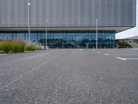 an empty parking lot next to a metal and glass building on a sunny day with lots of windows