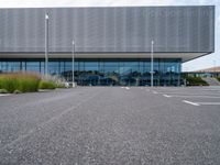 an empty parking lot next to a metal and glass building on a sunny day with lots of windows