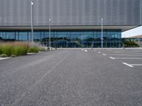 an empty parking lot next to a metal and glass building on a sunny day with lots of windows