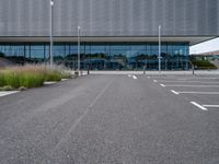 an empty parking lot next to a metal and glass building on a sunny day with lots of windows