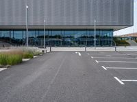 an empty parking lot next to a metal and glass building on a sunny day with lots of windows