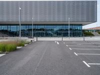 an empty parking lot next to a metal and glass building on a sunny day with lots of windows