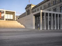 the large, empty sidewalk with multiple columns in front of the building with two signs