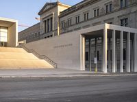 the large, empty sidewalk with multiple columns in front of the building with two signs