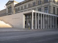 the large, empty sidewalk with multiple columns in front of the building with two signs