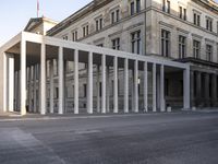 the large, empty sidewalk with multiple columns in front of the building with two signs