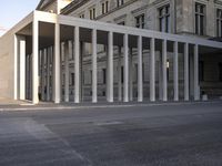 the large, empty sidewalk with multiple columns in front of the building with two signs