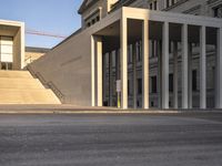 the large, empty sidewalk with multiple columns in front of the building with two signs