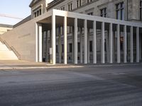 the large, empty sidewalk with multiple columns in front of the building with two signs