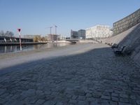 two benches in the street by a canal with buildings in the background in the city