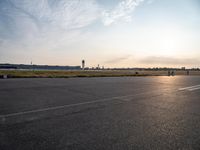 a picture of an airport runway with cars parked and a few planes flying in the background