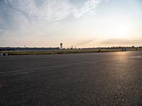 a picture of an airport runway with cars parked and a few planes flying in the background