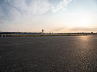 a picture of an airport runway with cars parked and a few planes flying in the background