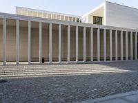 an empty courtyard with multiple columns that are filled with bricks and stone steps, at a building structure