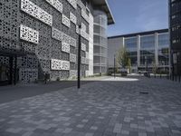 an empty bricked outdoor space has a walkway and large, modern building with geometric patterns