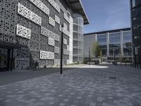 an empty bricked outdoor space has a walkway and large, modern building with geometric patterns