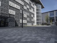 an empty bricked outdoor space has a walkway and large, modern building with geometric patterns