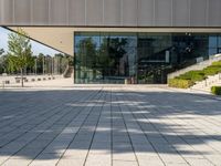 an empty courtyard on a sunny day, with the glass doors open and there is steps going up to the building