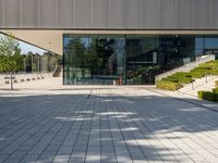 an empty courtyard on a sunny day, with the glass doors open and there is steps going up to the building