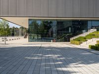 an empty courtyard on a sunny day, with the glass doors open and there is steps going up to the building