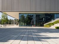 an empty courtyard on a sunny day, with the glass doors open and there is steps going up to the building