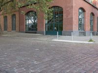 brick paved sidewalk and entrance to old red brick building with green doors in city area