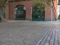 brick paved sidewalk and entrance to old red brick building with green doors in city area