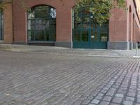 brick paved sidewalk and entrance to old red brick building with green doors in city area