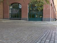 brick paved sidewalk and entrance to old red brick building with green doors in city area