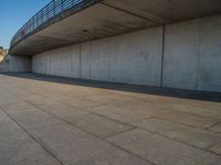 a skateboarder riding on a cement ramp next to a city street under a bridge