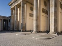 a street corner with several pillars and people walking in front of it and cars parked by