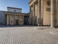 a street corner with several pillars and people walking in front of it and cars parked by